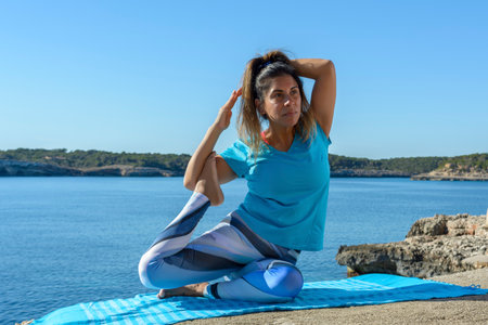 middle-aged fitness woman outdoors in front of the sea does yoga stretching exercisesの写真素材