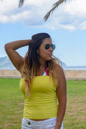 portrait of a latin woman smiling, having fun, on vacation in mallorca posing on a warm spring summer day, under a palm tree, hollidays conceptの写真素材