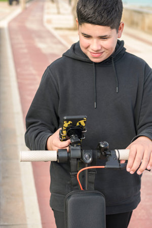 Front view 14-17 years old smiling happily riding electric scooter on the bike lane and using smart phone music apps, E-Mobility urban leisure conceptの写真素材