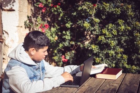 young latin man reads book in front of laptop, outdoorsの写真素材
