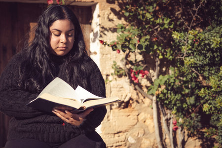 young latin woman sitting reading a bookの写真素材