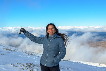 portrait of latin woman smiling in the snow, with warm clothes above the clouds, on the top of the...