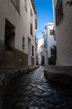 A narrow pathway with a small stream and white buildings on either side under a bright blue sky, Alpujarras, granada, andalucia, espa aの写真素材