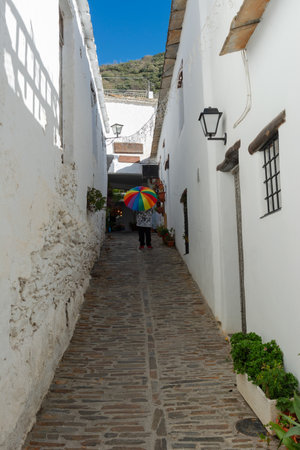 Narrow cobblestone alley lined with white buildings, person holding a colorful umbrella in a sunny scene, Alpujarras, granada, andalucia, espaÃ±aの写真素材