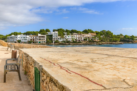 Coastal town with modern buildings and a stone promenade under a partly cloudy sky, porto petro, mallorca balearic islands, spainの写真素材