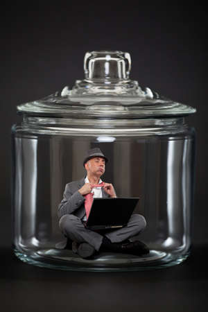 Businessman trapped inside a transparent glass jarの写真素材