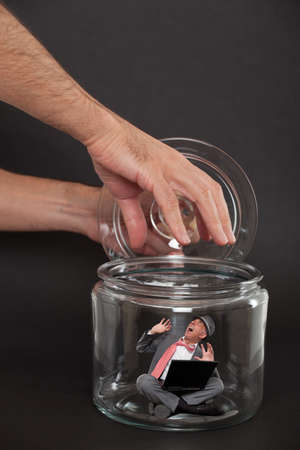 Businessman trapped inside a transparent glass jarの写真素材
