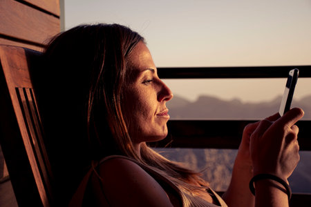 Woman resting with her mobile phone at sunsetの写真素材