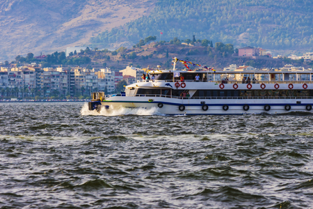 The ferry boat is navigating in the sea in front of the turkish city of Izmir (Turkey), during the sunsetのeditorial素材