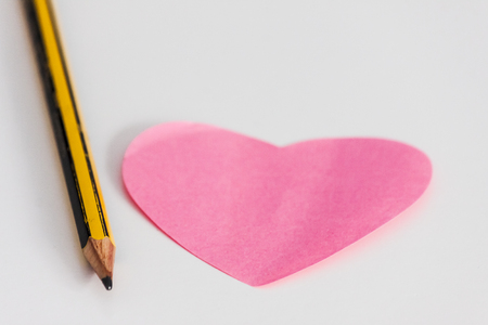Pink heart note and pencil on white deskの写真素材