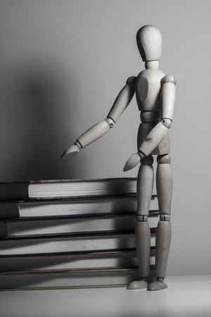 Wooden puppet standing near a stack of book, on a white deskの写真素材