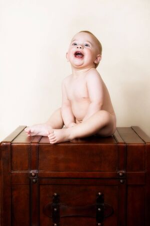 Young baby sitting on an old style suitcaseの写真素材