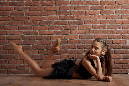 Girl in black skirt lying near brick wallの写真素材