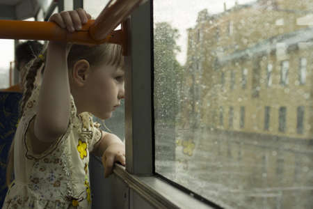 Little girl looking throw tram window at the rainの写真素材