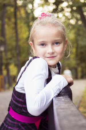 Little preteen girl standing near railing in park at autumnの写真素材