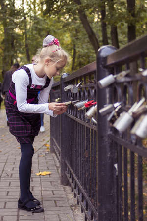 Little preteen girl examines the lock on the railing in park at autumnの写真素材