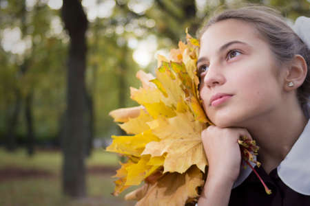 nice young teenage schoolgirl with autumn leaves looking into the distance  in the parkの写真素材