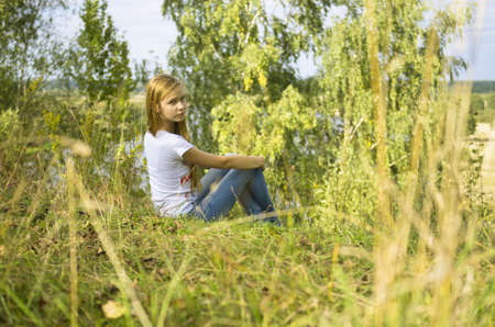 young girl sitting in the grass at the autumnの写真素材