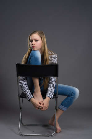 nice teenage girl jeans posing in studio in jeans and shirt on the chairの写真素材