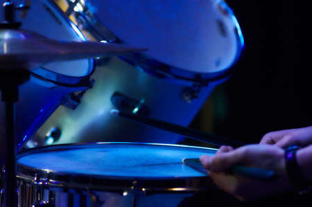man playing drum kit at a concert in the blue LED lights