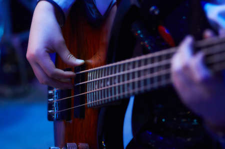girl hands play bass guitar at a concert under blue soft light