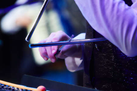 girl hands play triangle at a concert under blue soft lightの写真素材