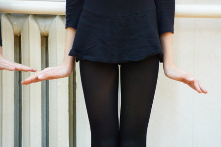 A girl dancer in black clothing stands with outstretched arms next to an old decorative radiator, appearing to balance themselves in an interior settingの写真素材