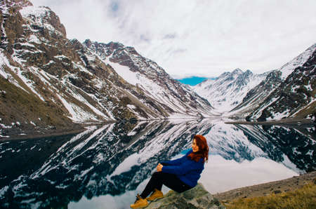 Redhead young adult woman posing in front of Andes Mountains with a blue jacket and looking at the camera.の写真素材