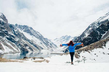 A young adult woman posing with open arms while appreciating the view of the Andes Mountains in Portillo, Chile.の写真素材