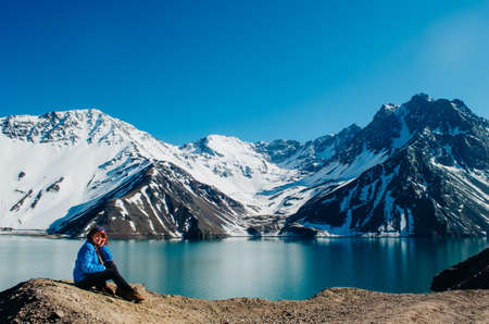 A young adult woman sitting and smiling and looking to the camera enjoying the view of El Yeso Dam in the Andes Mountains.の写真素材
