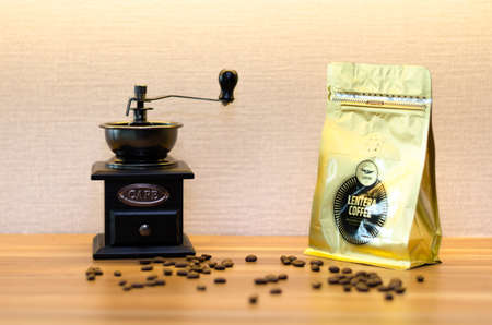 A coffee grinder with an open drawer and messy coffee beans on a wood table.のeditorial素材