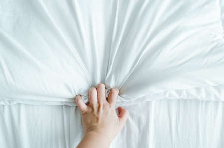 Hand expressing emotions while holding white wrinkly sheets in the bed.