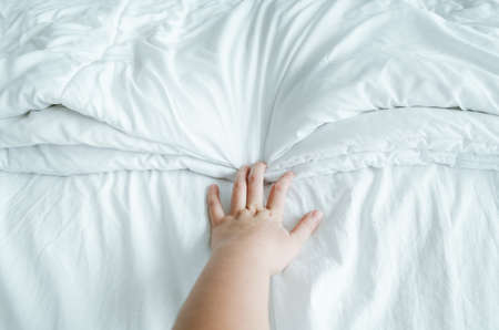 Hand expressing emotions while holding white wrinkly sheets in the bed.