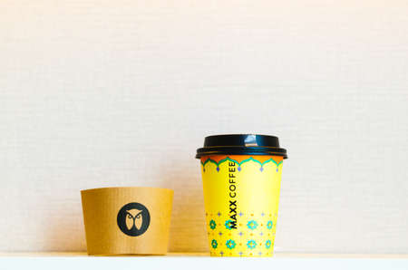 A yellow take away cup of coffee with the Maxx Coffee chain owl logo in the center of the heat...