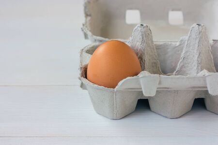Close-up of a single brown egg in a carton on white background