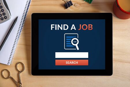Find a job concept on tablet screen with office objects on wooden desk. All screen content is designed by me. Top viewの写真素材