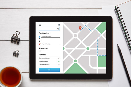 Location tracker concept on tablet screen with office objects on white wooden table. GPS map...
