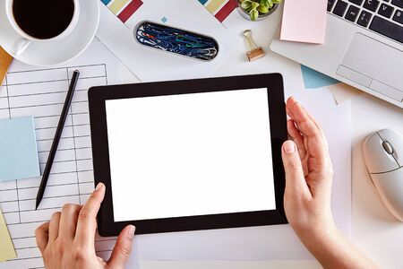 Mockup image of hands using a digital tablet computer with blank white screen on business desk. Top...