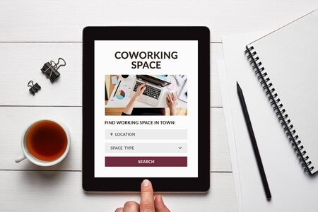 Coworking space concept on tablet screen with office objects on white wooden table. Top viewの写真素材