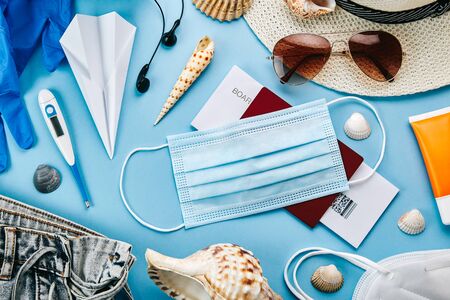 Overhead view of coronavirus travel accessories on blue background. Essential summer vacation items during the coronavirus pandemic. Covid-19 and travel concept.の写真素材