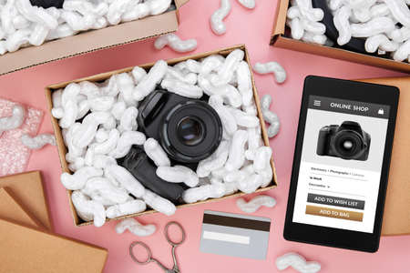 Tablet computer with online shop app on screen surrounded by parcels with protective foam pads and...
