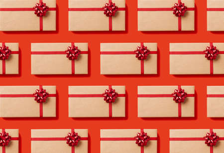 Overhead view of seamless pattern of Christmas gift boxes wrapped in craft paper with a red bow on red background.の写真素材
