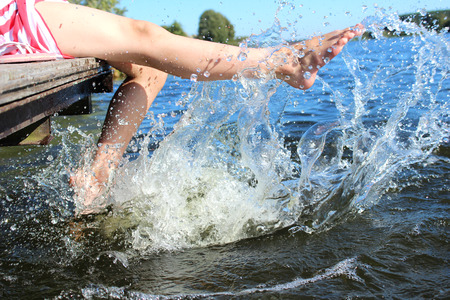 The girl on the dock by the lake swinging his legs making splashesの写真素材