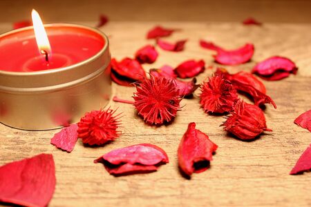 burning red candle on the table with petals and flowersの写真素材