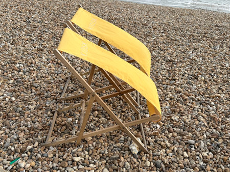 Wooden beach chair on pebble beach with yellow warning sign