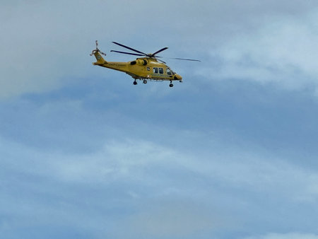 Helicopter in flight against a blue sky with white clouds.