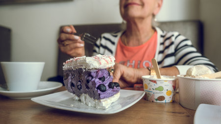 In a cafe. Colorful cake, ice cream and coffee on the table. Hand of an elderly woman with a cake...