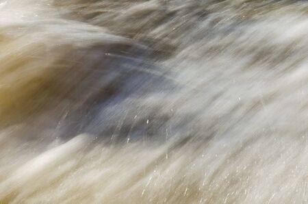 Texture of fast moving water, in yellowish soft tones. Flow, smoothness, motion.