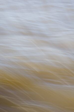 Texture of fast moving water, in yellowish soft tones. Flow, smoothness, motion.