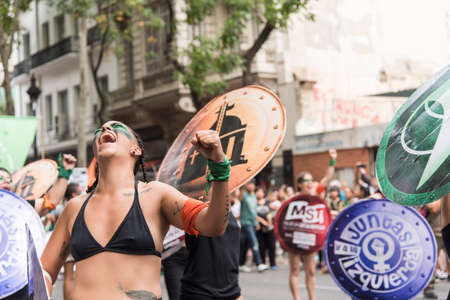 CABA, Buenos Aires / Argentina; March 9, 2020: international women's day. Young woman, shouting, with a green and an orange symbolic handkerchiefs: legal abortion and Church / State separationのeditorial素材